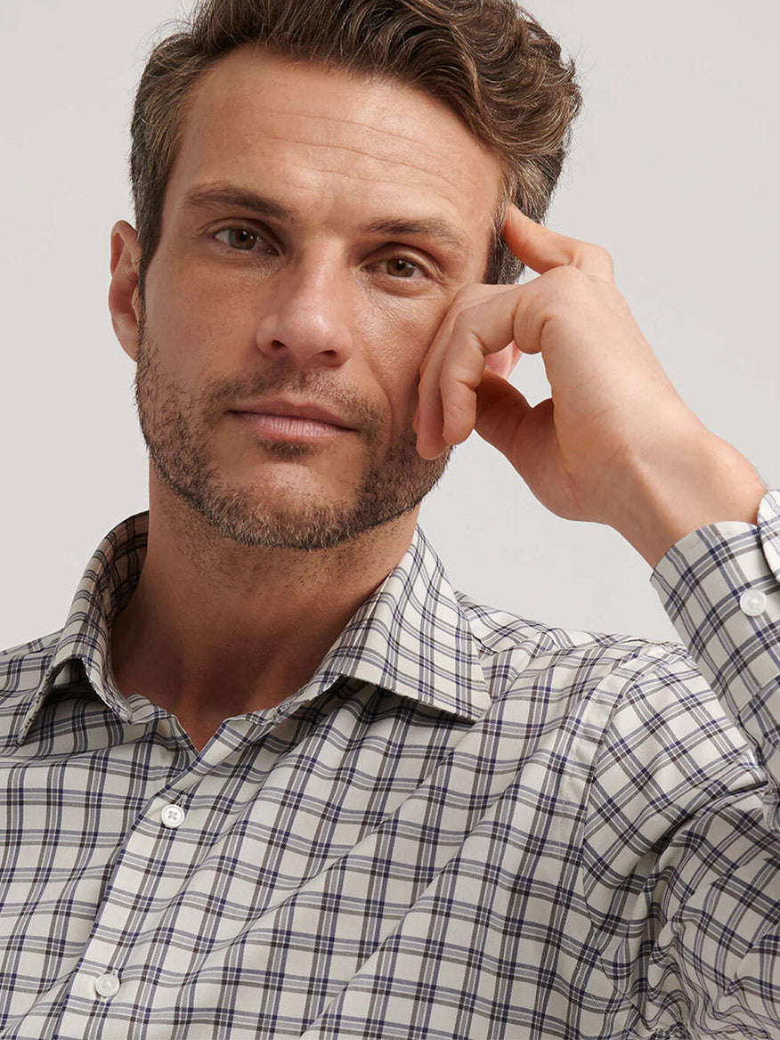 A man with short hair and light stubble wears the Peter Millar Lenox Crown Lite Cotton-Stretch Sport Shirt in Winter Ivory and rests his hand on his face, looking at the camera.