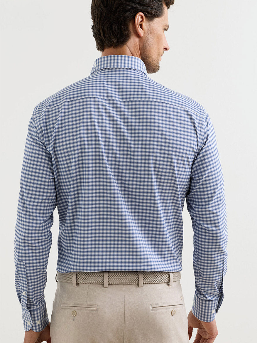 Man facing away, wearing the Peter Millar Lewis Performance Twill Sport Shirt in Windsor Blue and beige pants with a patterned belt, set against a plain light background.