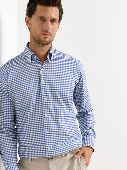 A man wears the Peter Millar Lewis Performance Twill Sport Shirt in Windsor Blue and beige pants, standing against a plain white background.