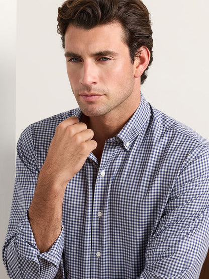A man wearing a navy and white gingham Peter Millar Liam Crown Soft Twill Sport Shirt in Navy with a button-down collar.
