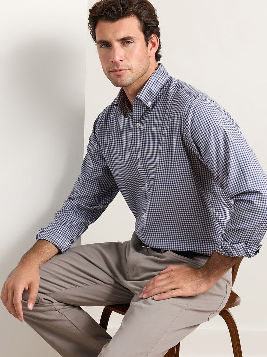 A man wearing a Peter Millar Liam Crown Soft Twill Sport Shirt in Navy and light-colored trousers sitting on a wooden chair.