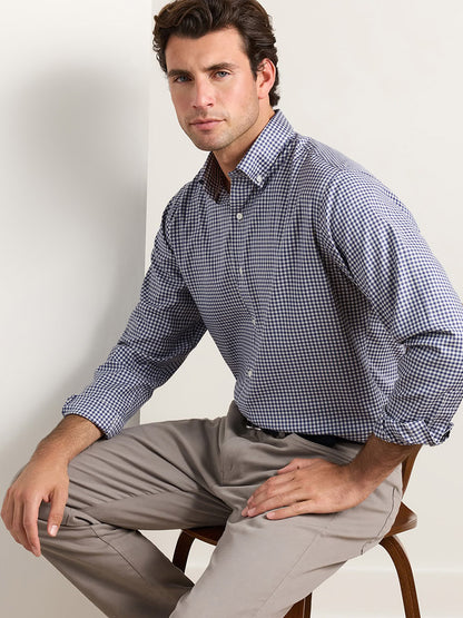 A man wearing a Peter Millar Liam Crown Soft Twill Sport Shirt in Navy and light-colored trousers sitting on a wooden chair.