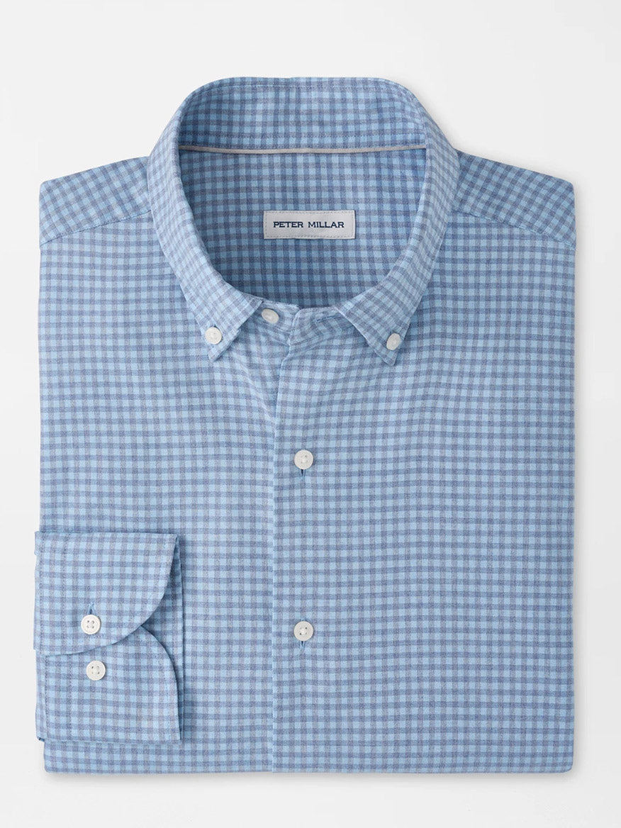 The Peter Millar Liam Crown Soft Twill Sport Shirt in Blue Freesia is a folded light blue and white checkered shirt featuring a collar, white buttons, and the signature "Peter Millar" label inside the collar. Crafted from easy-care, stretch performance fabric, it offers all-day comfort and effortless style.