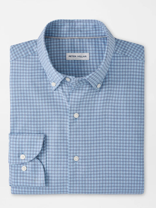 The Peter Millar Liam Crown Soft Twill Sport Shirt in Blue Freesia is a folded light blue and white checkered shirt featuring a collar, white buttons, and the signature "Peter Millar" label inside the collar. Crafted from easy-care, stretch performance fabric, it offers all-day comfort and effortless style.