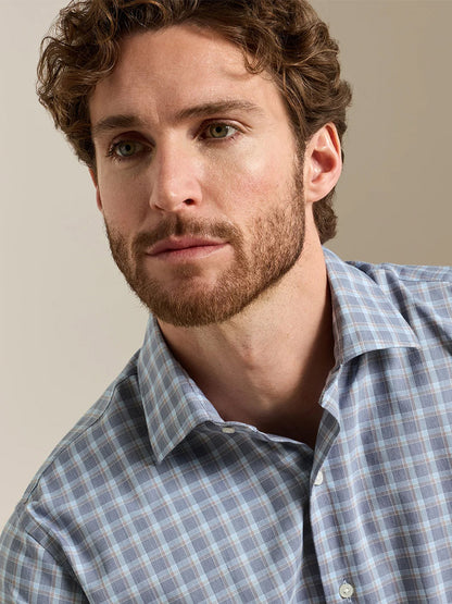 A man with brown hair and a beard wears the Peter Millar Lincoln Crown Lite Cotton-Stretch Sport Shirt in Navy, featuring a blue and white checked pattern and classic fit, as he looks slightly to the side against a plain background.