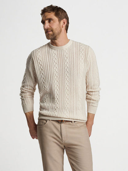 A man wearing the Peter Millar Crescent Ridge Cable Crew in Winter Ivory and beige pants stands against a plain white background, showcasing perfect 3-season wear.