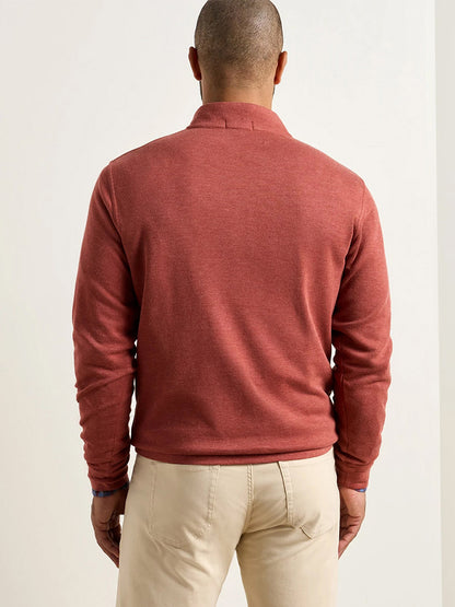 A person stands facing away, wearing the Peter Millar Crown Comfort Pullover in Burnt Orange—a lightweight, long-sleeved quarter-zip—paired with beige pants, set against a plain light background.