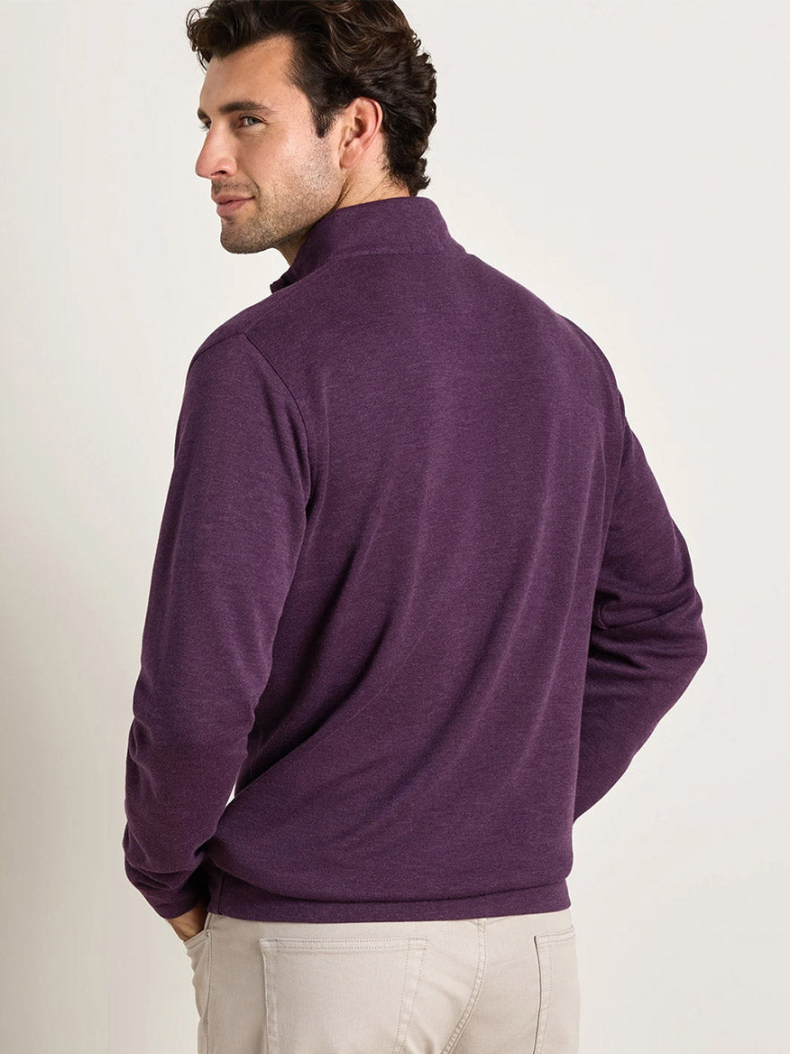 A man is seen from behind, looking over his shoulder, wearing the Peter Millar Crown Comfort Pullover in Grapeseed—a long-sleeve, lightweight quarter-zip featuring four-way stretch—paired with light-colored pants.