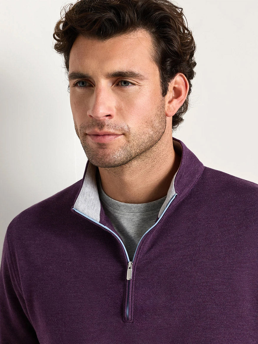 A man with short brown hair and light stubble wears the Peter Millar Crown Comfort Pullover in Grapeseed—a lightweight, four-way stretch quarter-zip—over a gray shirt, looking slightly to the side.
