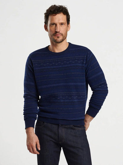 A man in a navy Peter Millar Midnight Fairisle Crewneck Sweater and jeans stands against a plain background.