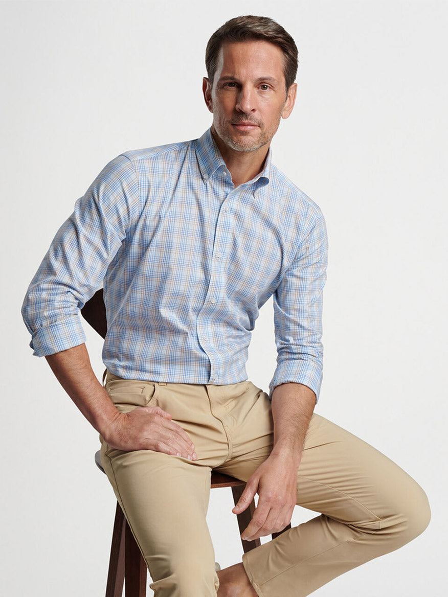 Man seated on stool wearing a Peter Millar Milo Cotton Sport Shirt in Blue Frost, and khaki trousers.