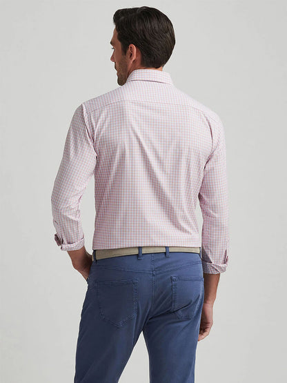 A man wearing the Peter Millar Mingus Performance Poplin Sport Shirt in Pink Crepe and blue pants stands against a gray background, highlighting style and performance.