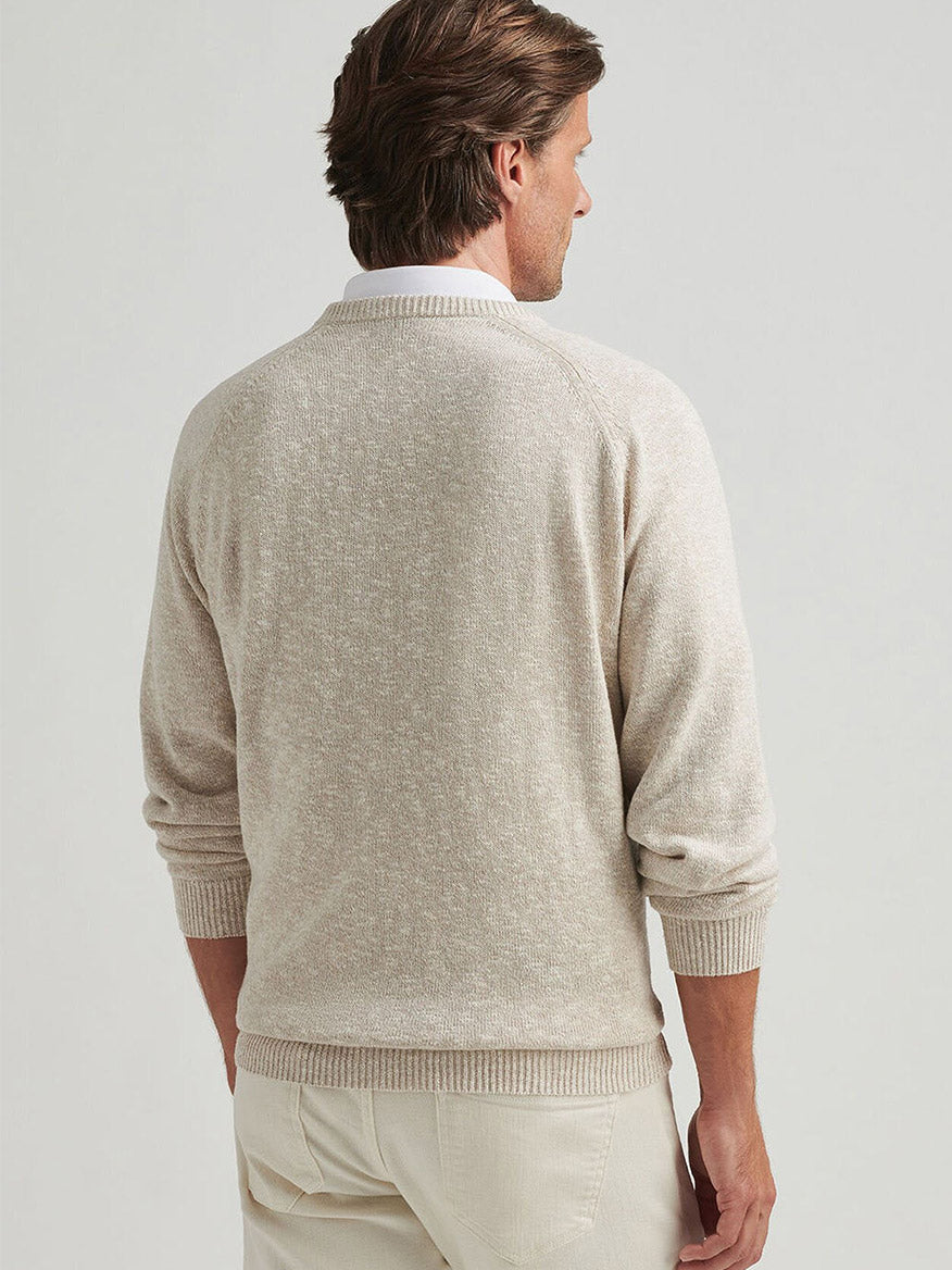 A person with brown hair wears a Peter Millar Montauk V-Neck Sweater in Palm Thatch, featuring raglan sleeves, paired with light-colored pants, standing with their back to the camera against a plain background.