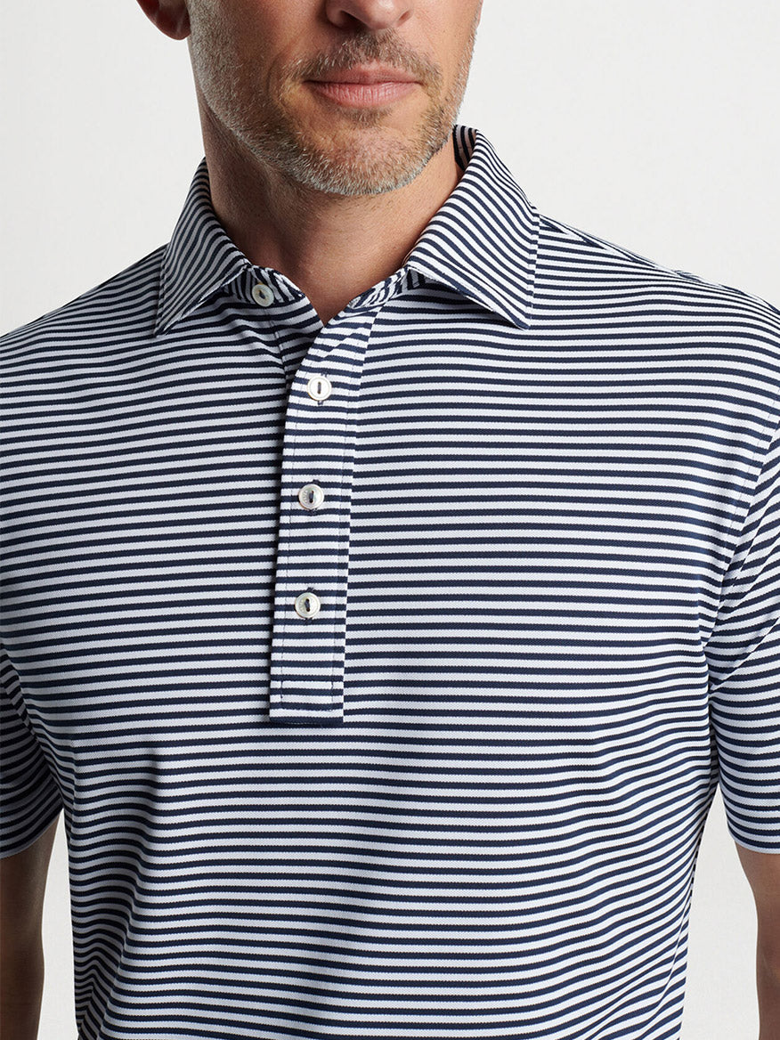 A man wearing a striped, button-up Peter Millar Mood Performance Mesh Polo in Navy.