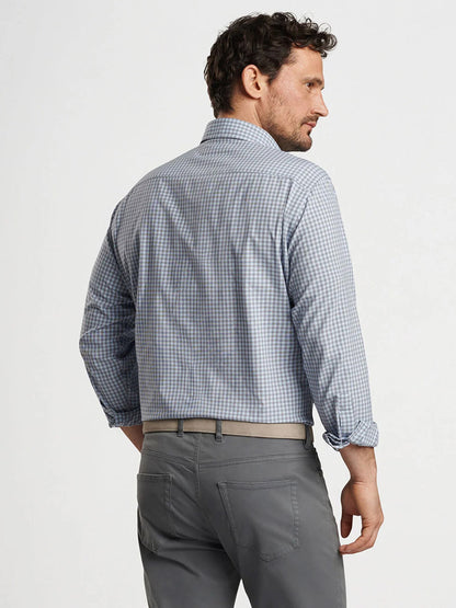 A man with short, curly hair and a beard is wearing a navy checkered Peter Millar Murray Performance Poplin Sport Shirt and gray pants. He is standing and looking over his left shoulder.