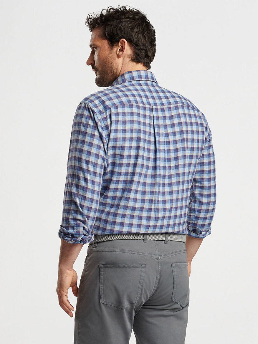 A man in a Peter Millar North Bay Cotton Sport Shirt in Ocean Blue, featuring a classic fit and blue checkered pattern with rolled-up sleeves, is facing sideways. He pairs the shirt with gray pants and has short dark hair.