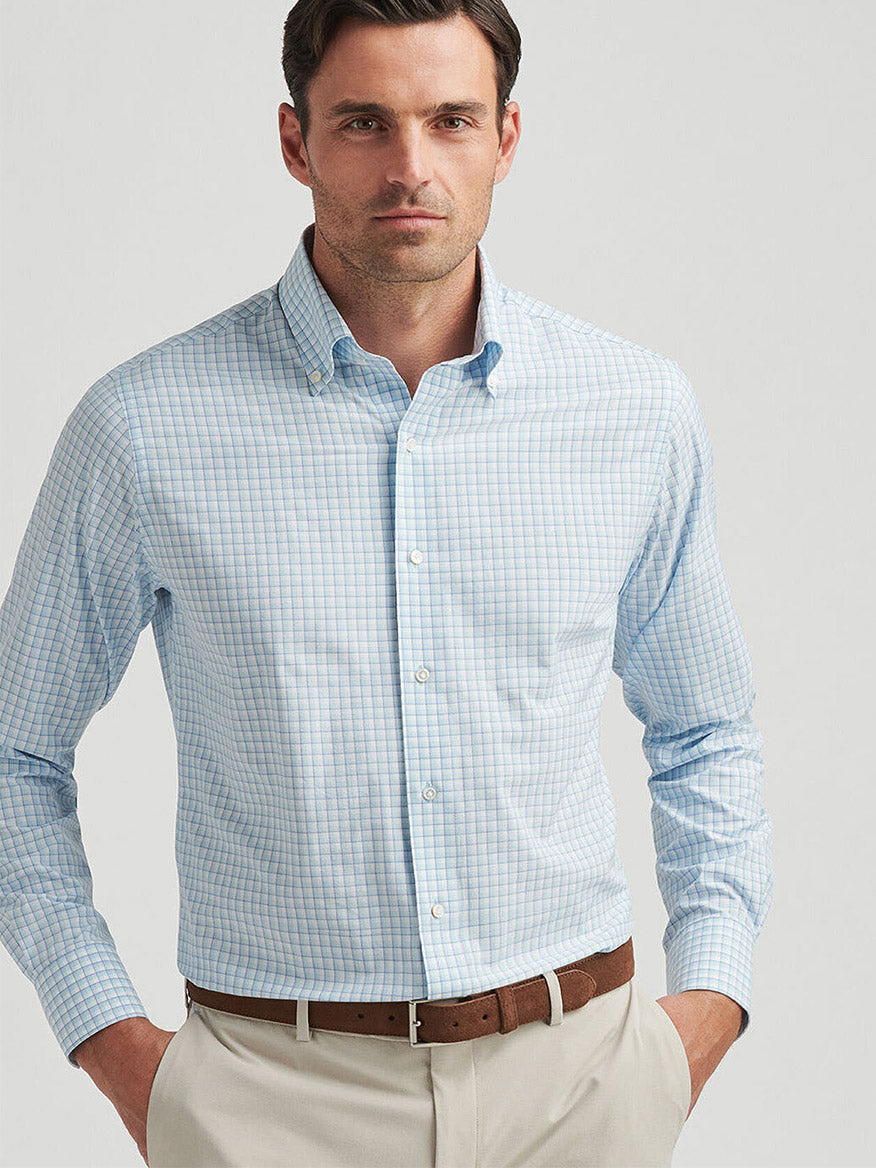 A man stands confidently, wearing a Peter Millar Parker Performance Poplin Sport Shirt in Blue Spruce and beige pants, hands in pockets, looking forward.