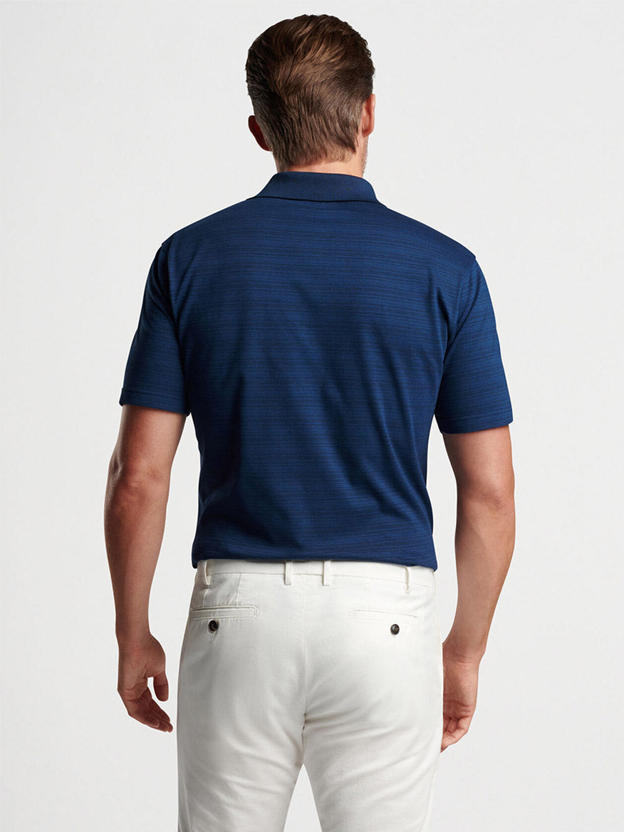 Man viewed from behind wearing a Peter Millar Pembroke Polo in Blue Pearl and white pants, standing against a simple light background.
