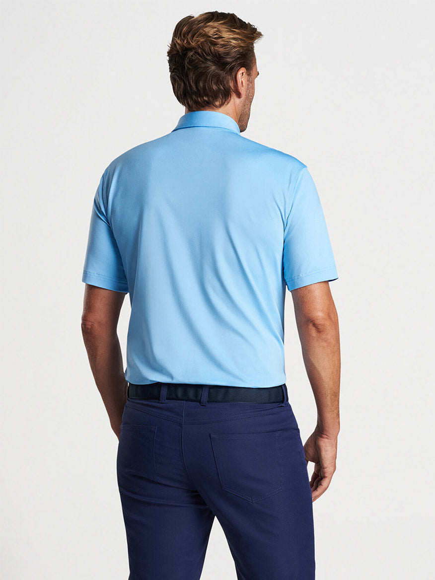Man wearing a Peter Millar Solid Performance Jersey Polo in Cottage Blue [Sean Self Collar] and navy pants on a golf course, viewed from the back.