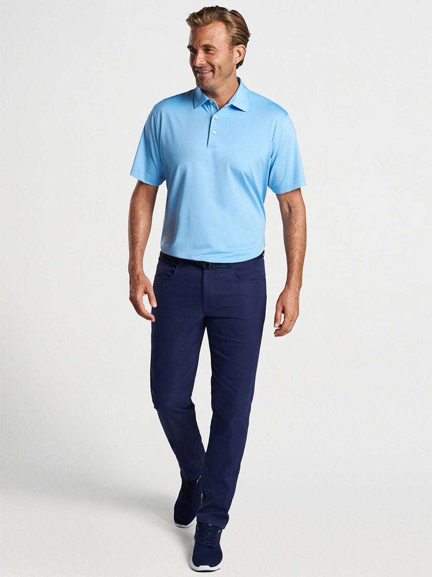 Man walking casually on the golf course in a Peter Millar Solid Performance Jersey Polo in Cottage Blue with a Sean Self Collar and dark trousers.