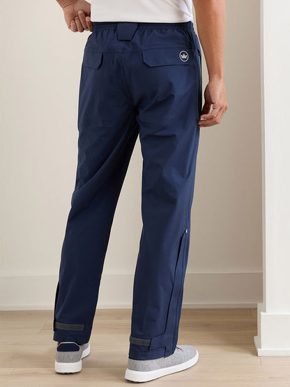 A person stands indoors wearing the Peter Millar Rain Walker Pant in Navy, featuring adjustable cuffs and back pockets, paired with a white shirt and gray slip-on shoes.
