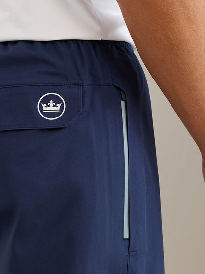 Close-up of a person wearing navy Peter Millar Rain Walker Pant, featuring a white crown logo above the back pocket and a vertical side zippered pocket, crafted from waterproof fabric for enhanced performance.