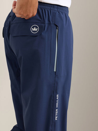 Close-up of a person wearing Peter Millar Rain Walker Pant in Navy, featuring a crown logo on the back pocket and a zippered side pocket for stylish, waterproof protection.