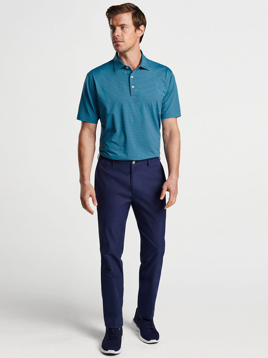 Man modeling a teal polo shirt and Peter Millar Raleigh Performance Trouser in Navy, crafted from moisture-wicking performance fabric.