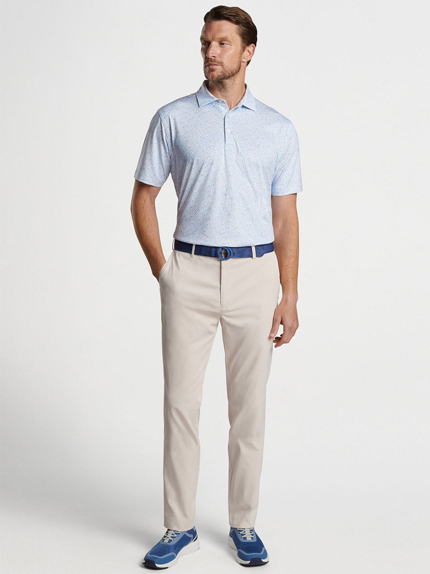 Man posing in a light blue patterned shirt, Peter Millar Raleigh Performance Trouser in Stone, and blue shoes.