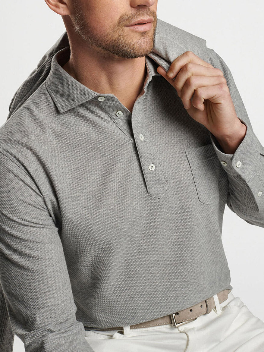 A man in a Gale Grey Peter Millar Ramble Long-Sleeve Cotton Cashmere Polo holds a jacket over his shoulder.