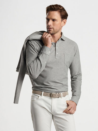 A man wearing a Peter Millar Ramble Long-Sleeve Cotton Cashmere Polo in Gale Grey and white pants, holding a jacket over his shoulder, gazes to the side.