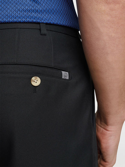Man wearing a blue shirt and Peter Millar Salem Performance Short in Black with a buttoned back pocket detail, featuring moisture-wicking and quick-dry properties.