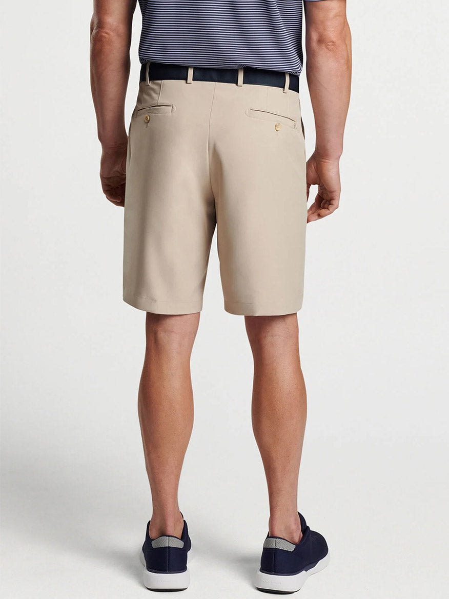 A man wearing Peter Millar Salem Performance Shorts in Khaki made of moisture-wicking performance fabric, a belt, and slip-on shoes stands with his back to the camera.