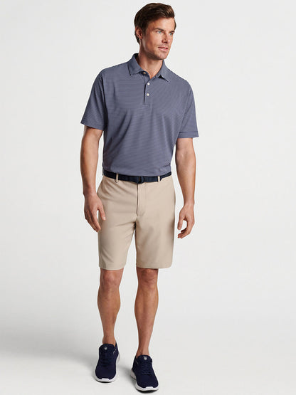 Man modeling casual attire with a gray moisture-wicking polo shirt, Peter Millar Salem Performance Short in Khaki, and blue sneakers.