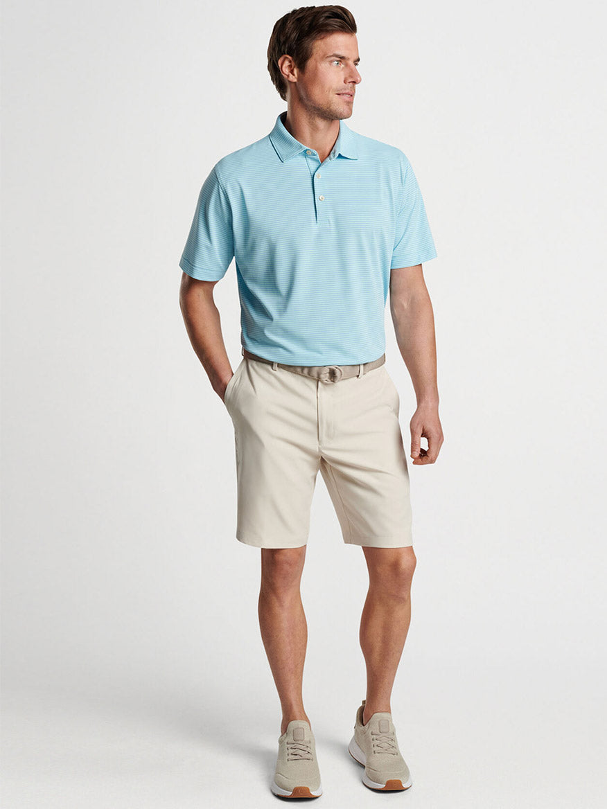 Man wearing a light blue polo shirt and beige Peter Millar Salem Performance Shorts in Stone, designed with moisture-wicking performance fabric, paired with a belt and casual shoes.