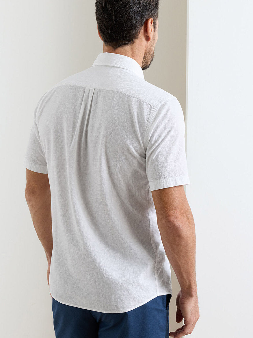 A man facing away from the camera wears a white Peter Millar Seaward Cotton Lyocell Sport Shirt and dark blue pants, standing near a white wall.