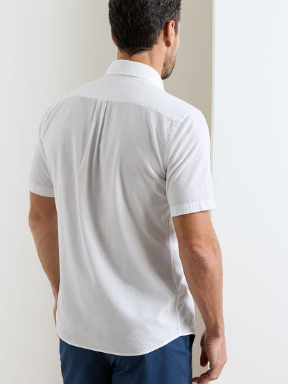 A man facing away from the camera wears a white Peter Millar Seaward Cotton Lyocell Sport Shirt and dark blue pants, standing near a white wall.