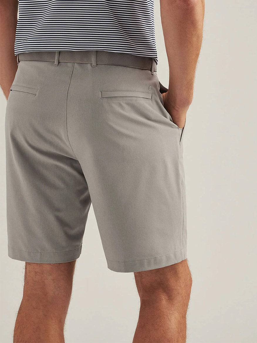 A person seen from behind wears the Peter Millar Shackleford Performance Hybrid Short in British Grey, featuring water-resistant fabric and back welt pockets, paired with a striped shirt.