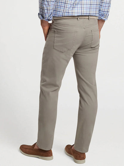 A person wearing a blue checkered shirt, Peter Millar Signature Sateen Five-Pocket Pant in Gale Grey, and brown shoes is seen from the back, with hands in their comfort waistband pockets.