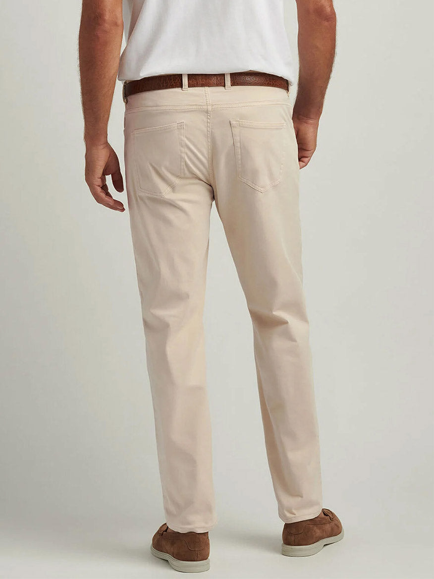 A man is shown from the back against a light background wearing Peter Millar Signature Sateen Five-Pocket Pant in Sand with a brown belt, white shirt, and brown shoes.