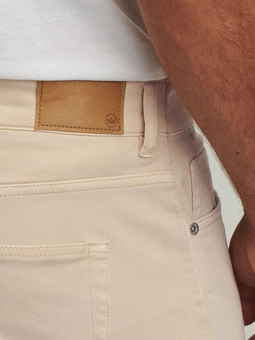 Close-up of the back of a person wearing Peter Millar Signature Sateen Five-Pocket Pant in Sand and a white shirt, featuring a brown leather patch on the waistband and visible pocket stitching for a classic fit.