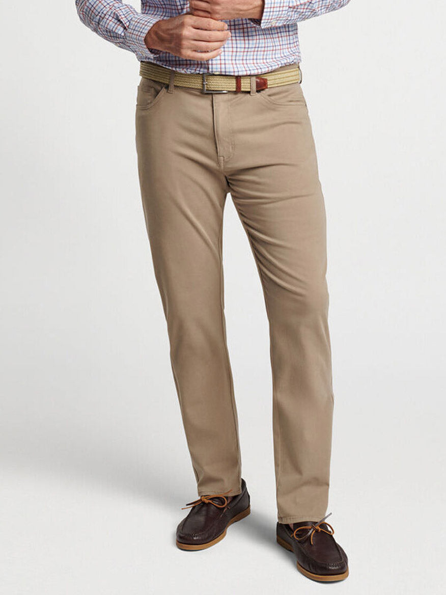 A person is wearing a light plaid shirt, the Peter Millar Signature Sateen Five-Pocket Pant in Grain, a beige woven belt, and dark brown leather shoes tied with brown laces. Only their torso and legs are visible.