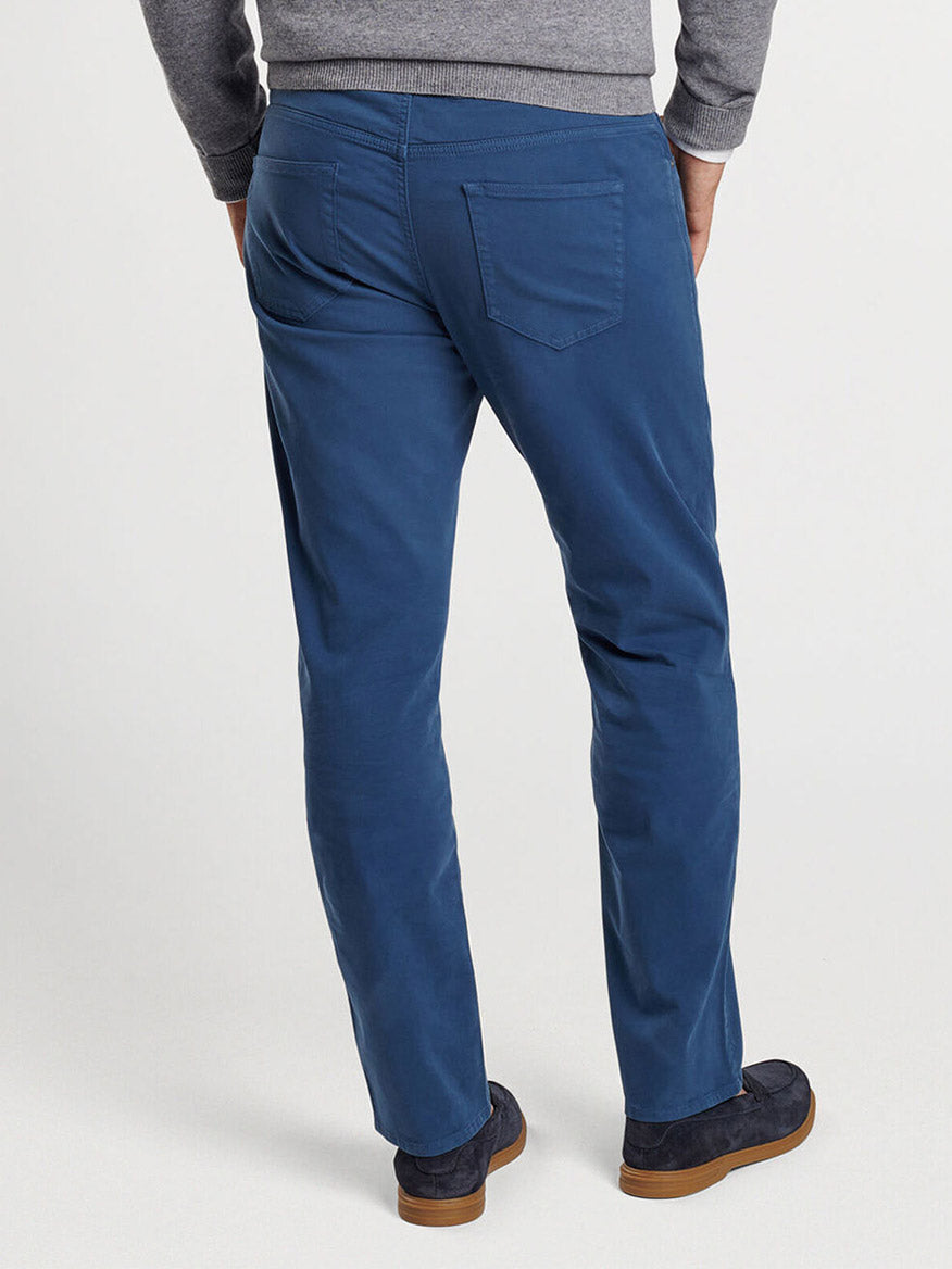 A person wearing a grey sweater and the Peter Millar Signature Sateen Five-Pocket Pant in Navy with hands in pockets, viewed from behind. The sophisticated ensemble is completed with dark blue shoes and a comfort waistband that adds to the lightweight feel of the outfit.