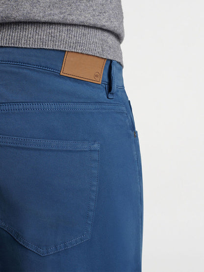 Close-up of a person wearing the Peter Millar Signature Sateen Five-Pocket Pant in Navy, featuring a visible back pocket and a brown leather label on the waistband, offering both a sophisticated look and comfort. A gray top edge is visible above the pants, highlighting their lightweight feel.