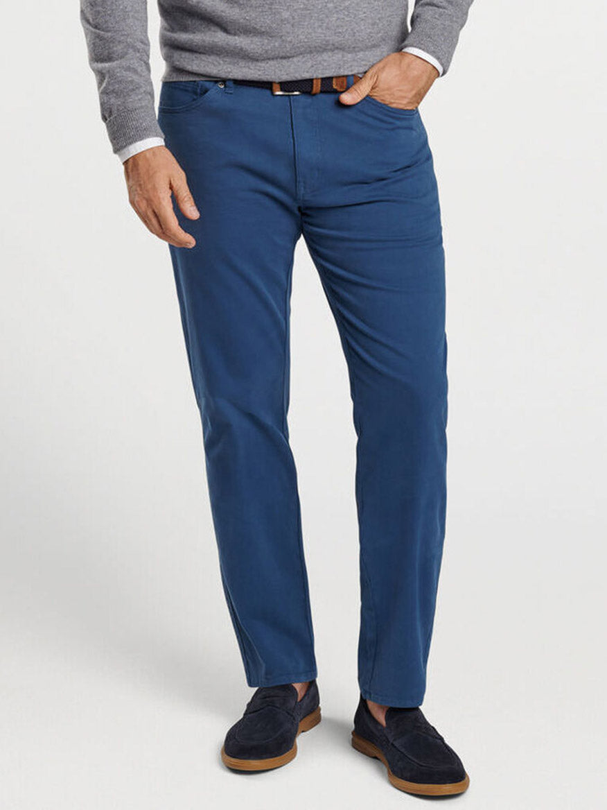 A person wearing a gray sweater, the Peter Millar Signature Sateen Five-Pocket Pant in Navy with a comfort waistband, and navy blue shoes. The person’s right hand is in their pants pocket.