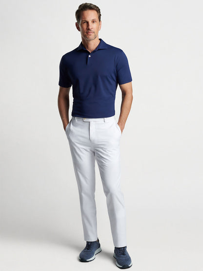 Man posing in a Peter Millar Solid Performance Jersey Polo in Navy shirt and white slacks with blue sneakers.