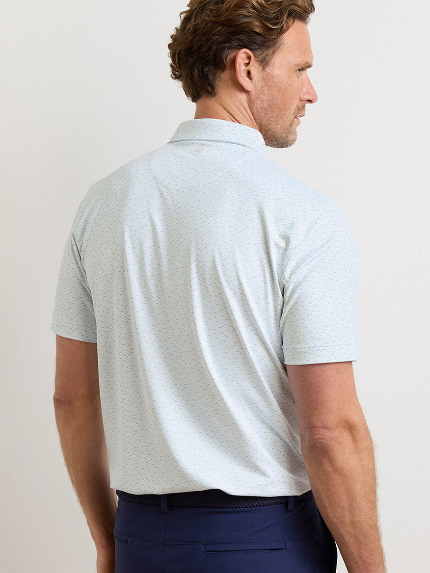 A man with short brown hair is shown from the back, wearing the Peter Millar Soprano Waves Performance Jersey Polo in White and dark blue pants.
