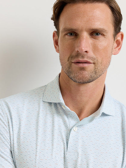 A man with short brown hair and light stubble wears the Peter Millar Soprano Waves Performance Jersey Polo in White, featuring UPF 50+ sun protection, standing against a plain light-colored background.