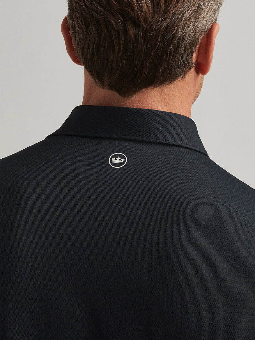 A person is seen from behind wearing a Peter Millar Soul Performance Mesh Polo in Black, distinguished by its dark color, four-way stretch material, and a small crown logo just below the collar.