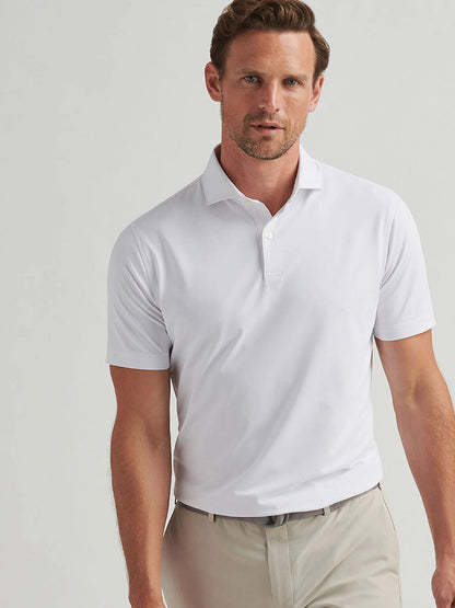 A man stands against a plain light background wearing the Peter Millar Soul Performance Mesh Polo in White and beige pants.